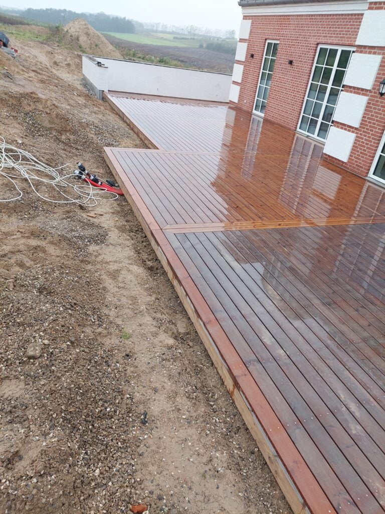 Nybygget træterrasse ved murstenshus i regnvejr