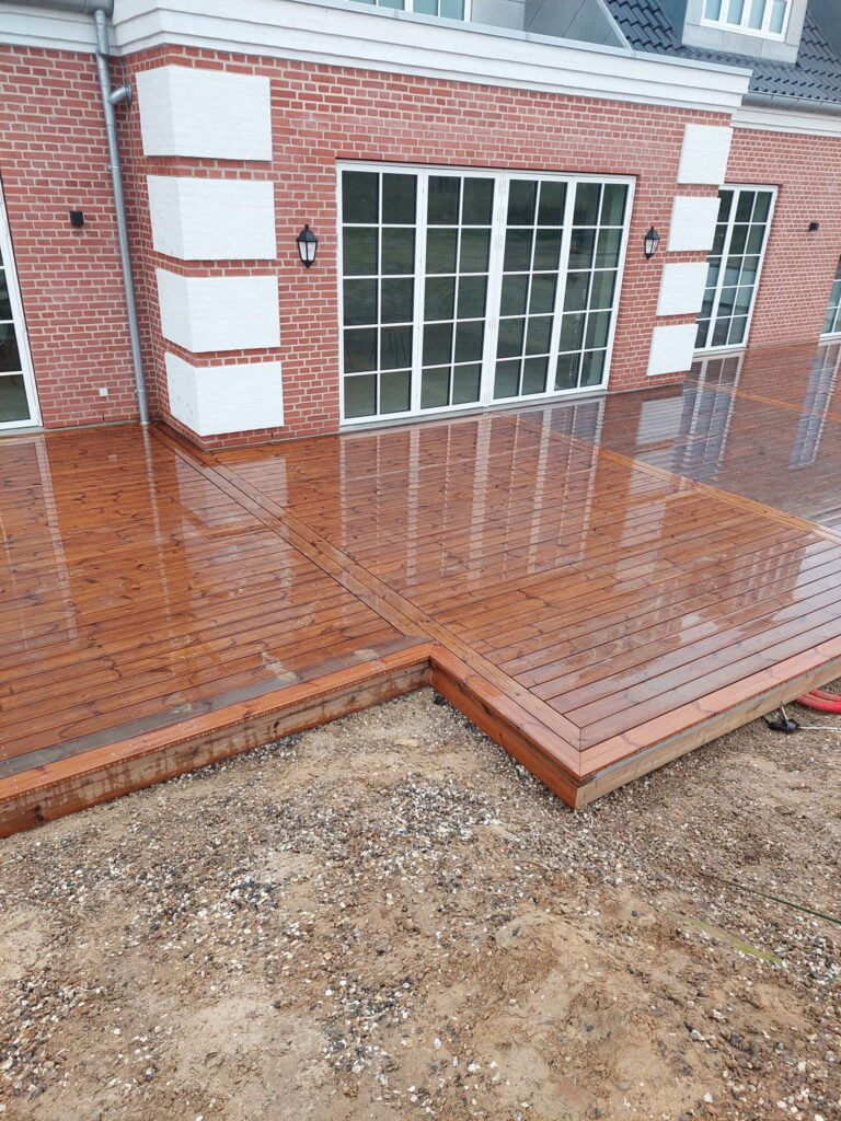 Nybygget træterrasse foran murstenshus med glasdøre