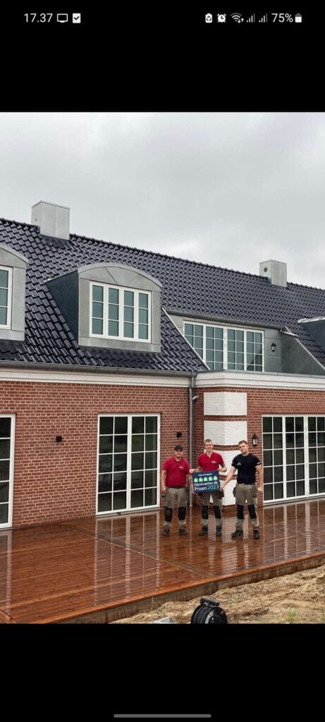 Håndværkere foran nybygget murstenshus med prisplakat