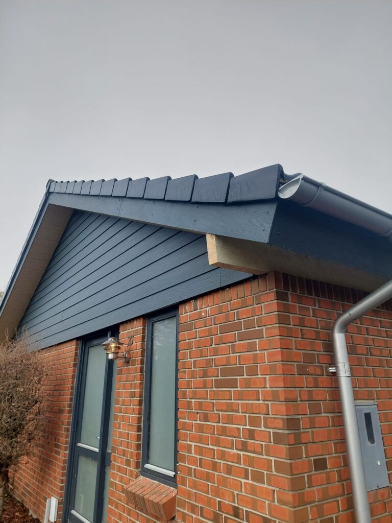 Murstenshus med blåt træværk og tagrende