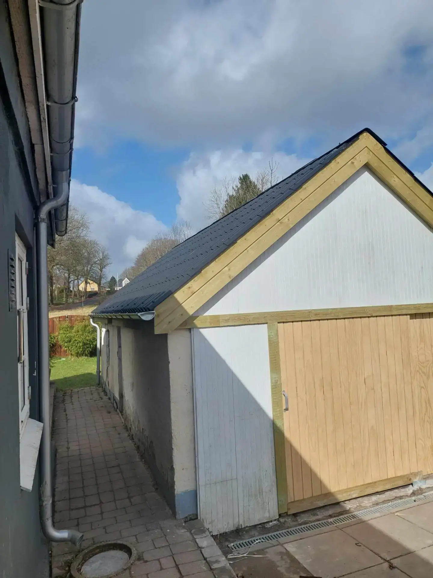 Nybygget hus med træfacade og sort tag under en skyet himmel.