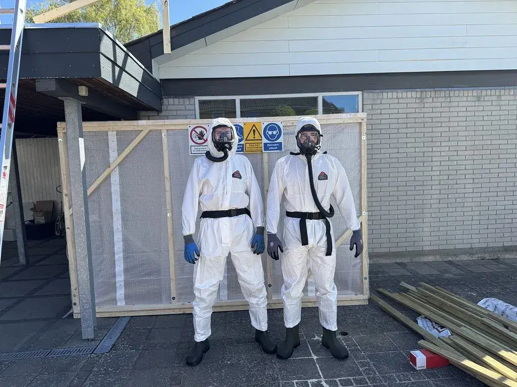 Bygningsarbejdere i beskyttelsesdragter foran byggepladsen.