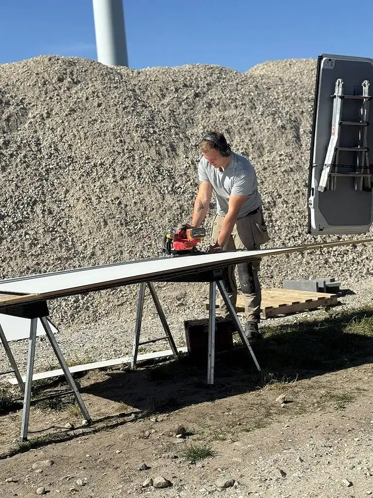 Mand arbejder med træmateriale på byggeplads med værktøj og udstyr.