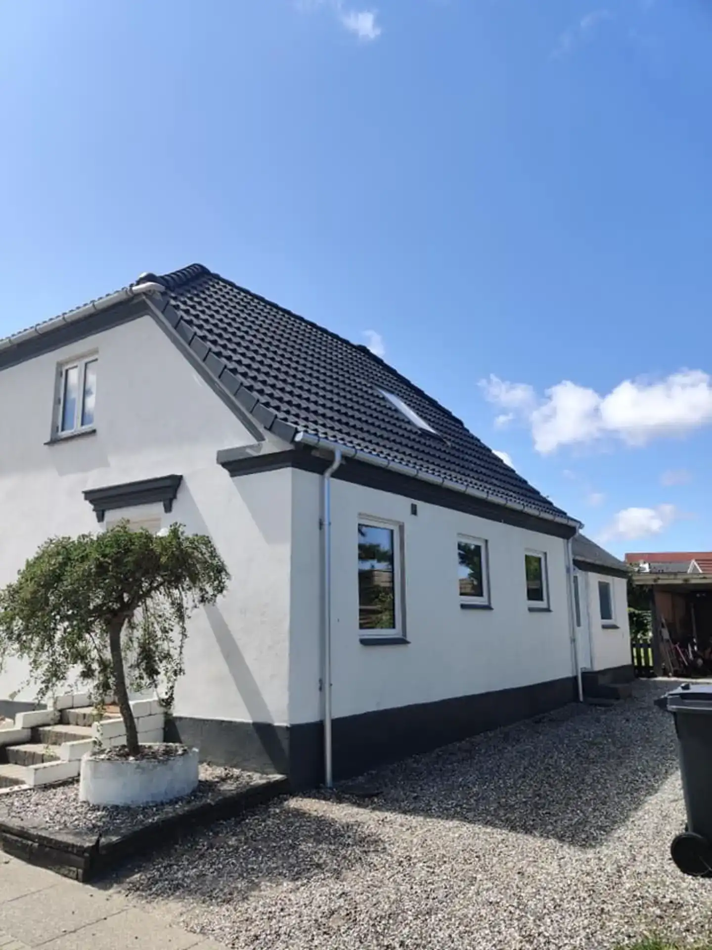 Hus med sort tag og hvid facade, moderne bolig med store vinduer og velplejet have.