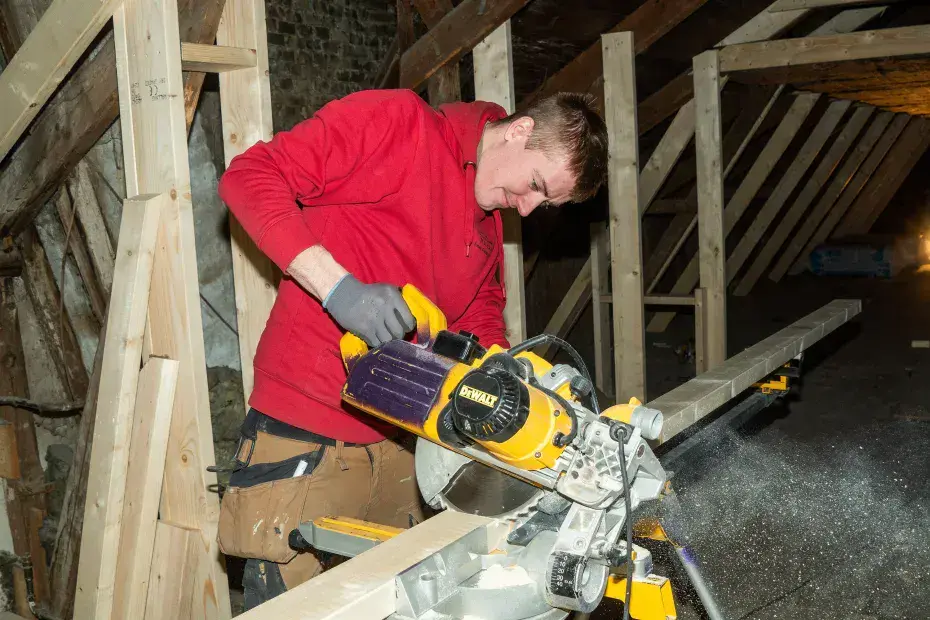 Mand arbejder med rundsav på tagkonstruktion i træ.