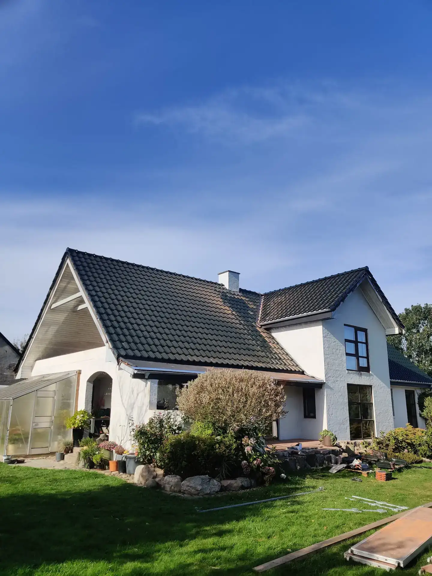 Hus med moderne design, store vinduer og velplejet have.