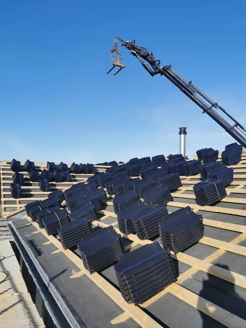 Billede af tagkonstruktion med sort tagsten og kran til installation af hegn eller havelåger.