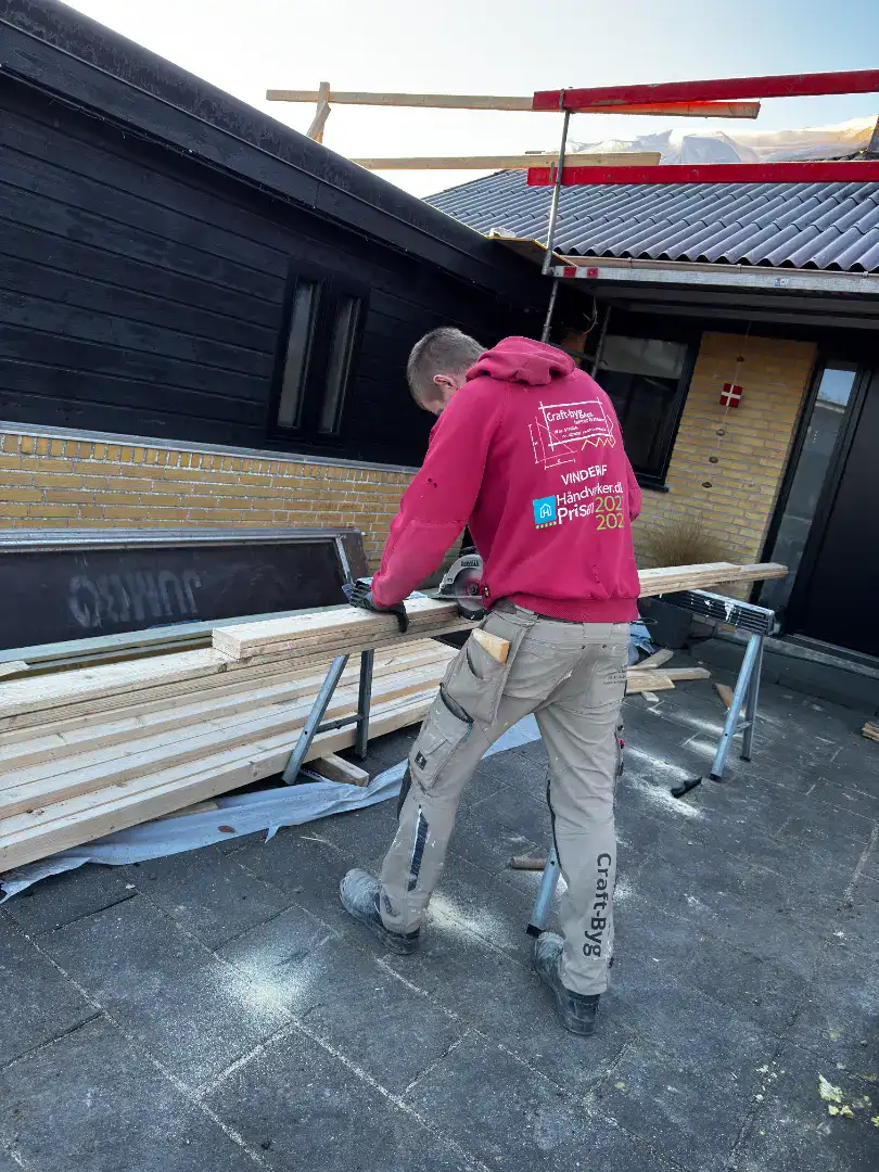 Håndværker skærer træ på byggepladsen foran et nyt hus under opførelse.